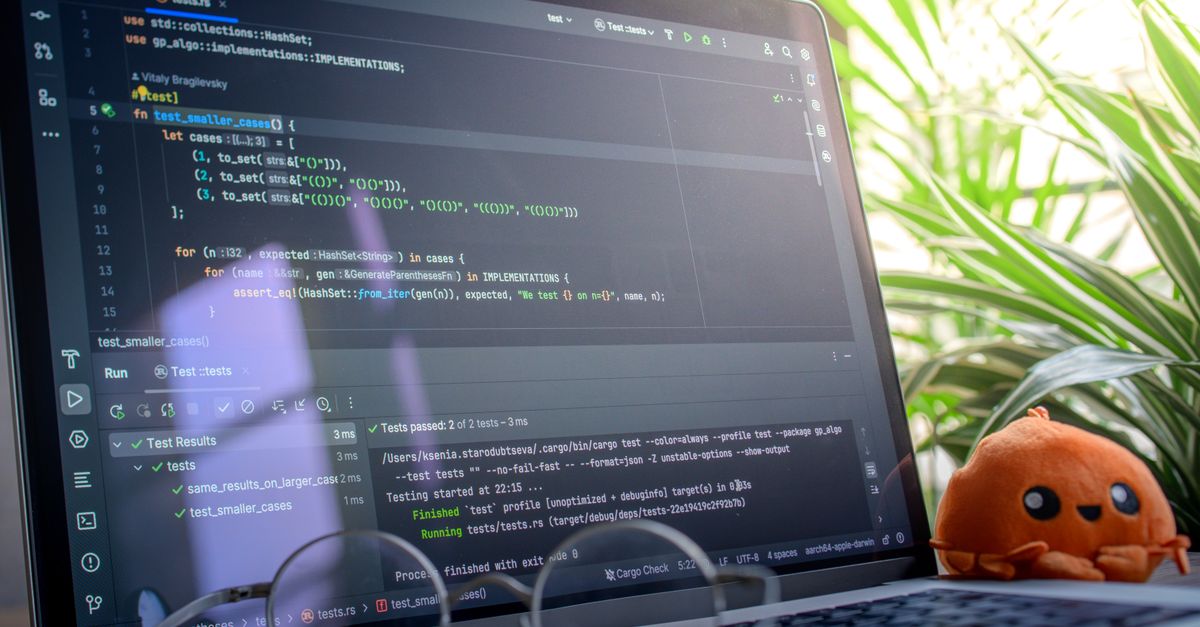 Open laptop displaying code next to a plush toy, set in a bright room with plants.