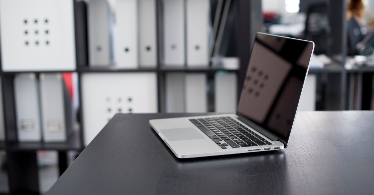 MacBook Pro displayed on a minimalist office desk with shelves in the background.